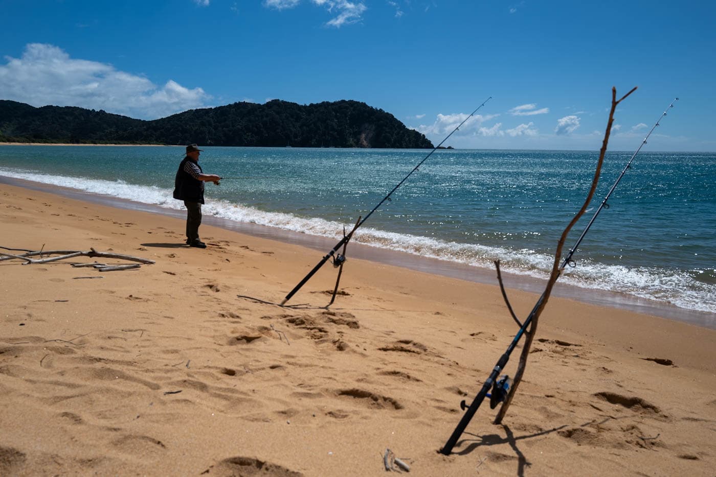 Person fishing from a quiet sandy beach with calm sea and wide sky in Golden Bay, New Zealand